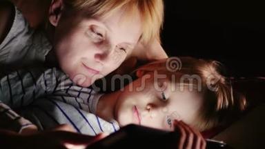 快乐的母亲和她的女儿。 我一起玩平板电脑，面对面躺在床上